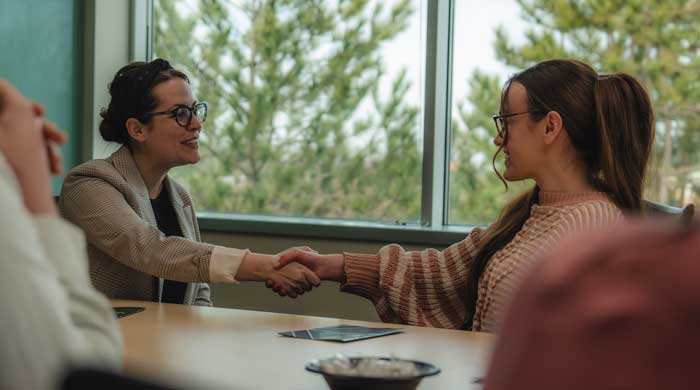 two women looking at each other speaking with a window behind them